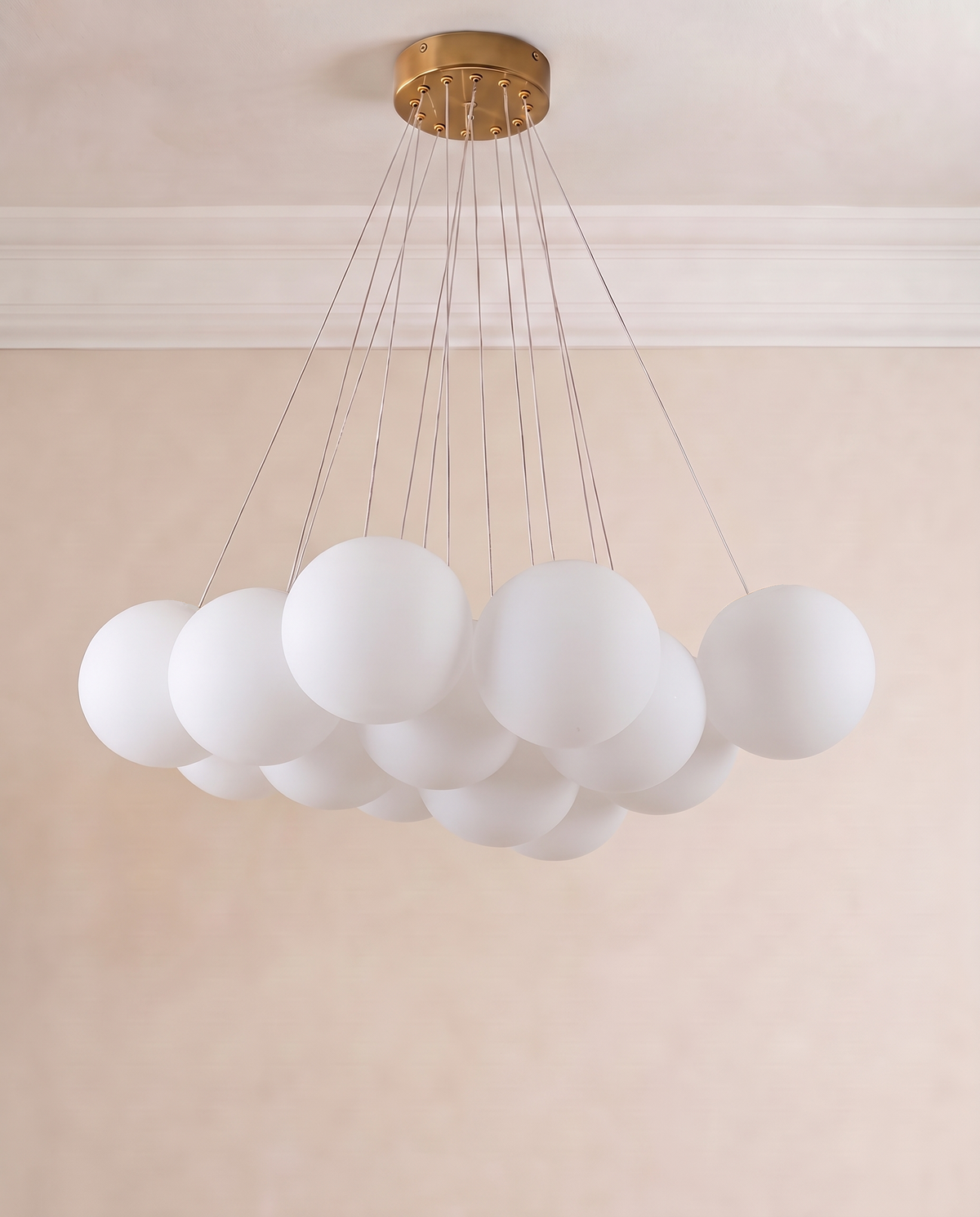 A modern cluster chandelier with multiple frosted white spherical acrylic shades suspended from a round brushed gold ceiling canopy by thin metal cables